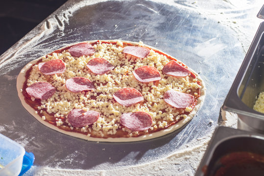Raw pizza with salami on stainles steel worktop