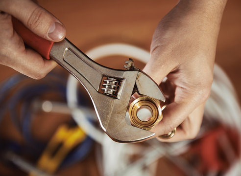 Close-up of plumber hands screwing nut of pipe with wrench over plumbing tools background. Concept of repair and technical assistance.  