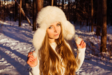 Happy pretty girl holding white fur hat in winter forest