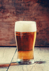 large glass of light beer with foam on the old wooden background