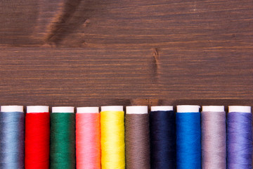 Row of sewing thread in different colors on wooden table