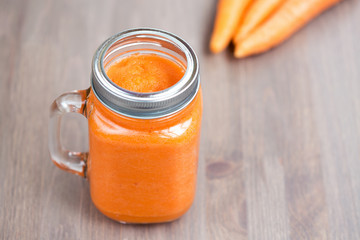 A carrot smoothie in a jar with carrots on wooden background