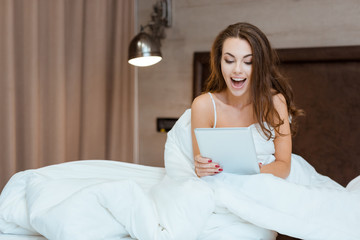 Cheerful woman using tablet computer on the bed
