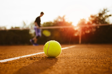 Tennis ball and silhouette of player on a clay court
