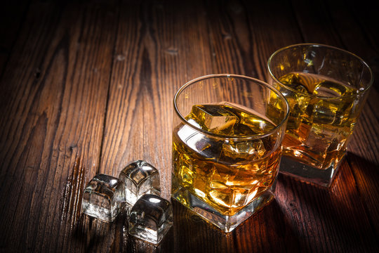 Two glasses of whiskey with ice on wooden table