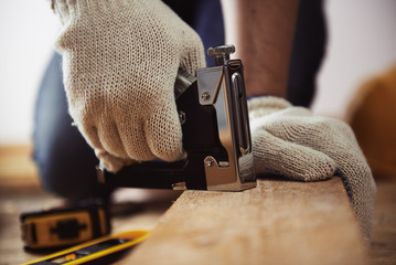 Male installer using stapler for wooden plank. Concept of home improvement.  - obrazy, fototapety, plakaty