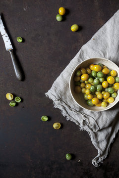 Overhead shot of yellow and green tomatoes on bowl on a rusty table with cloth and knife