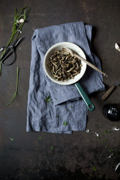 Overhead shot of cooked mushrooms in a pan on a rusty table with ingredients and tablecloth