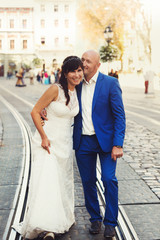 Naklejka premium bald groom and bride brunette walking on the streets of the old
