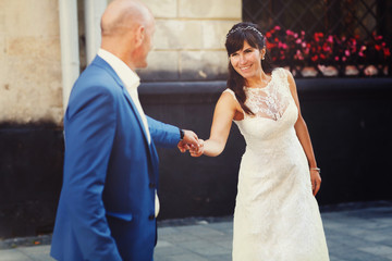 bride holding hands looking at the  groom on the streets of the