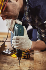 Male carpenter with drilling instrument working at home on the floor. Concept of house improvement and renovation.  - obrazy, fototapety, plakaty