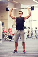 Fototapeta na wymiar young man flexing muscles with barbell in gym