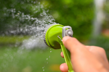Man's hand with garden hose watering plants