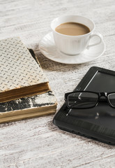 Books, coffee cup, glasses and e-book on white wooden table