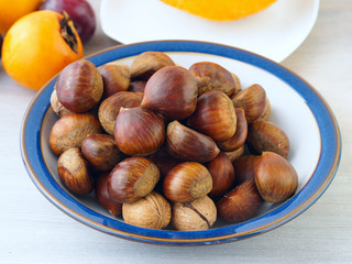 Wooden background with a plate with chestnuts and walnuts. Fall still life