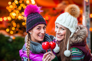 Frauen trinken Glühwein und essen Zuckerstangen auf deutschen Weihnachtsmarkt