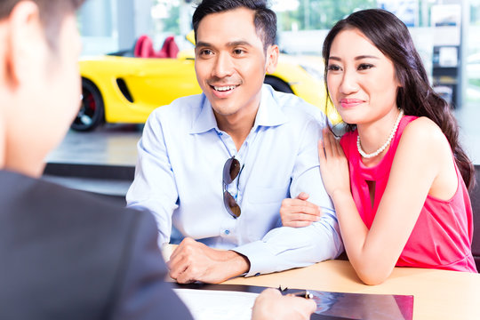 Asian Couple Signing Sales Contract For Car At Dealership