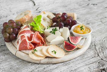 delicious appetizer to wine - ham, cheese, grapes, crackers, figs, nuts, jam, served on a light wooden board on  wooden surface