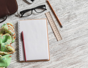 Open a blank Notepad, pen, glasses, phone, handbag and scarf on white wooden table