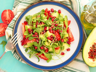 Vegetarian salad with avocado, tomato wedges, rucola leaves, pomegranate and sesame seeds
