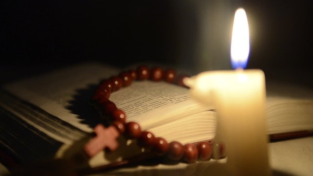 Candle burning on the background of the holy book and a cross