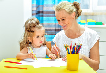 Young mother teaching little daughter draw pencils. Interior of