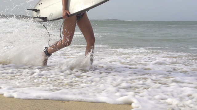 SLOW MOTION: Young female surfer running in shallow water