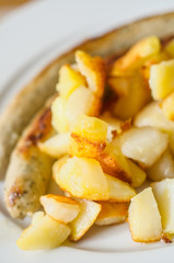 Fried potatoes with fried sausage on the white plate. 
