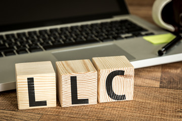 LLC (Limited Liability Company) written on a wooden cube in a office desk 