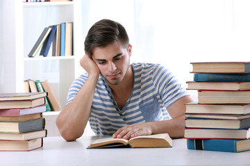 Young man reading book at table in room