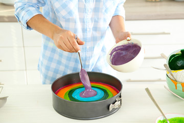 Young woman making rainbow cake in kitchen