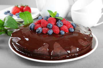 Delicious chocolate cake with summer berries on grey tablecloth, closeup
