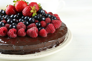 Delicious chocolate cake with summer berries on white wooden table, closeup