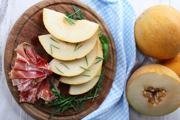 Melon with prosciutto of Parma ham on wooden table, closeup