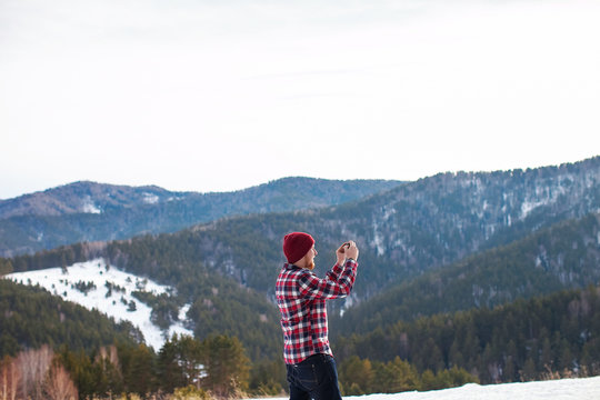 man in shirt and hat on the phone taking pictures in the mountains in winter