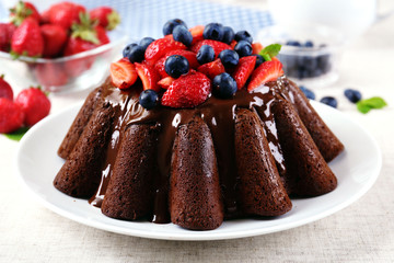 Tasty chocolate muffin with glaze and berries on table close up