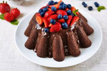 Tasty chocolate muffin with glaze and berries on table close up