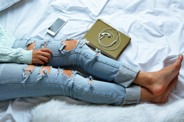 Woman in blue jeans with book and phone on bed top view point