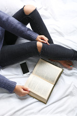 Obraz premium Woman in black jeans reading book on bed top view point