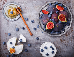 Fresh figs of different varieties; blueberries on a metal plate; brie cheese and honey.selective focus