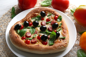 Delicious heart shaped pizza on the plate with vegetables around, close up