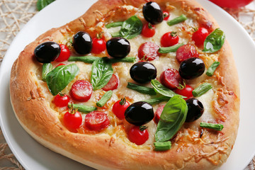 Delicious heart shaped pizza on the plate with vegetables around, close up