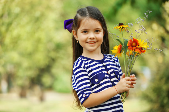 Portrait of happy little girl with flowers in park