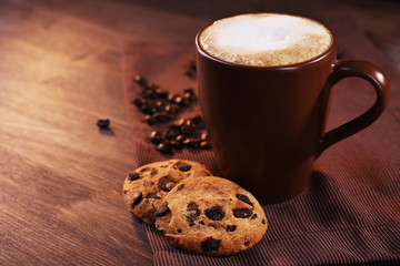 Cup of coffee, cookies with chocolate crumbs and roasted coffee beans on brown napkin on wooden background