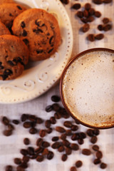 Cup of coffee, tasty cookies and coffee beans scattered on napkin, top view