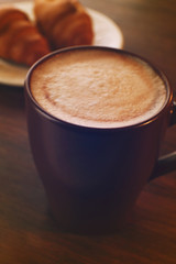 Cup of coffee with milk foam and croissant on wooden background