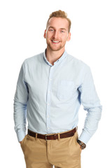 An attractive young man wearing a blue shirt with khaki pants, standing smiling towards camera against a white background.