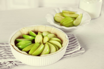 Woman making apple pie on wooden table, on light background