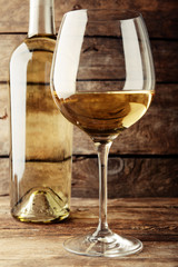 A bottle of white wine and a glass on wooden table