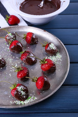 A plate of strawberries in chocolate on blue wooden background